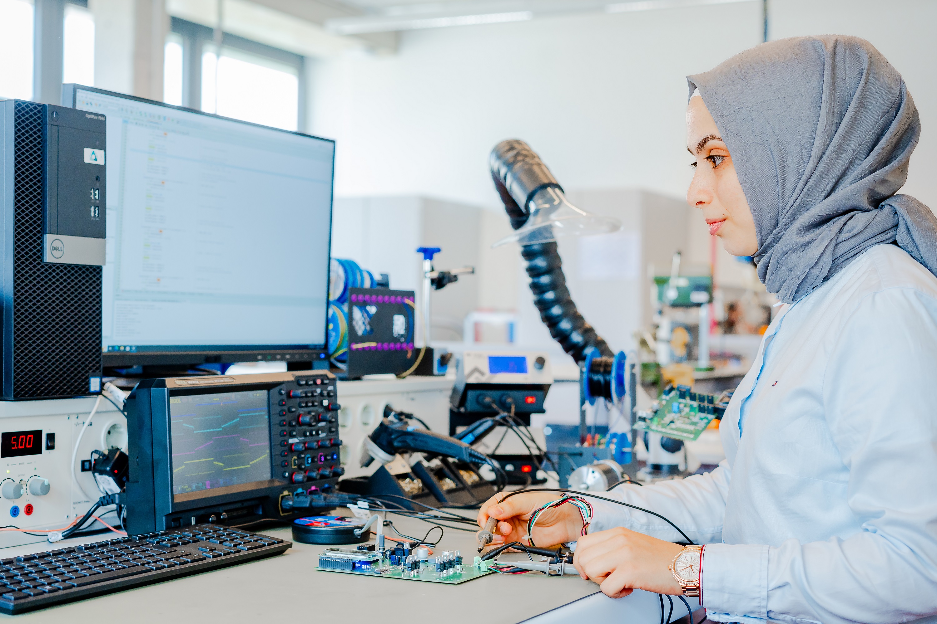 Weibliche Person mit hellem Kopftuch lötet im Lehrlabor