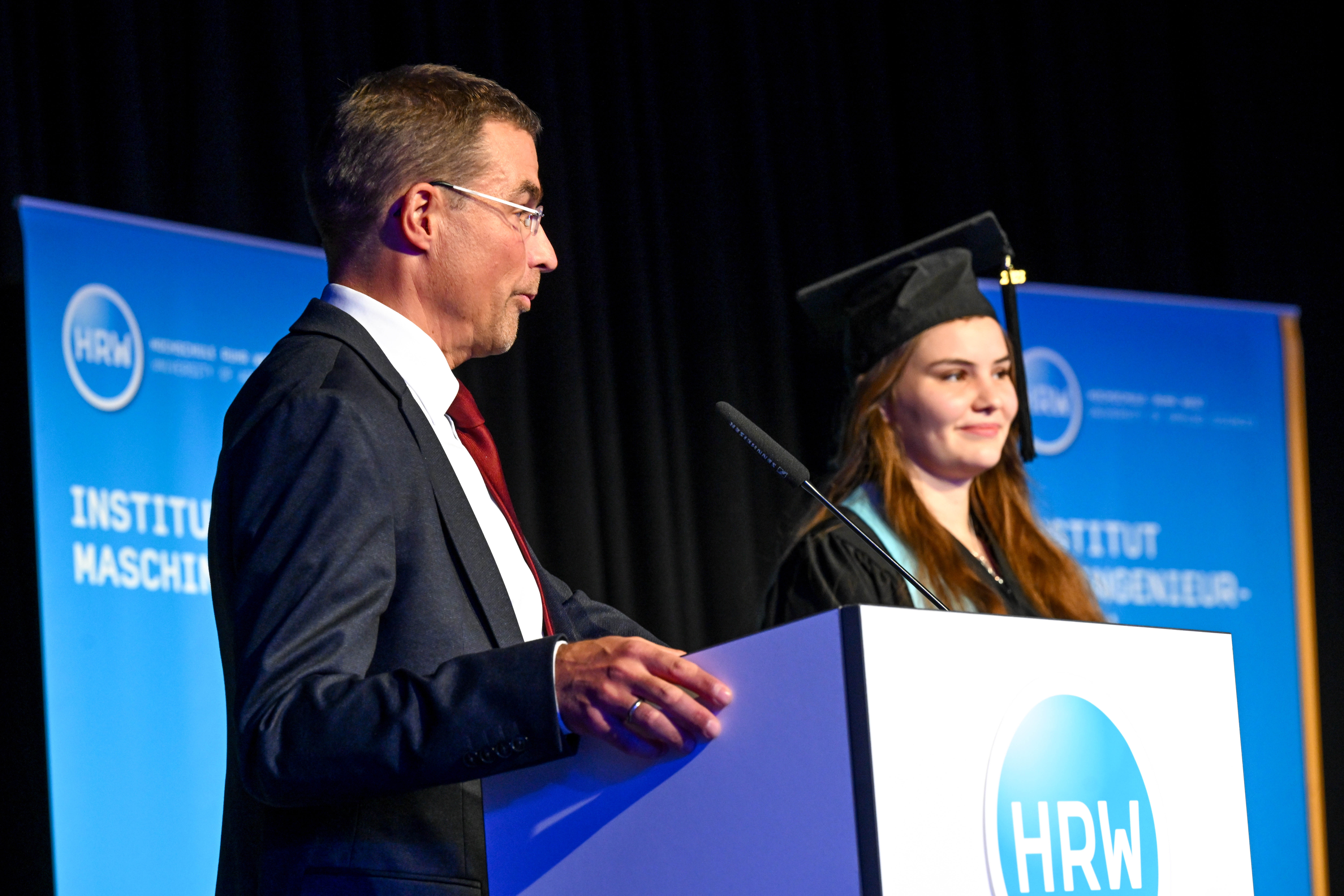 Professor Peer Heine hält eine Rede auf die neben ihm stehende Absolventin.