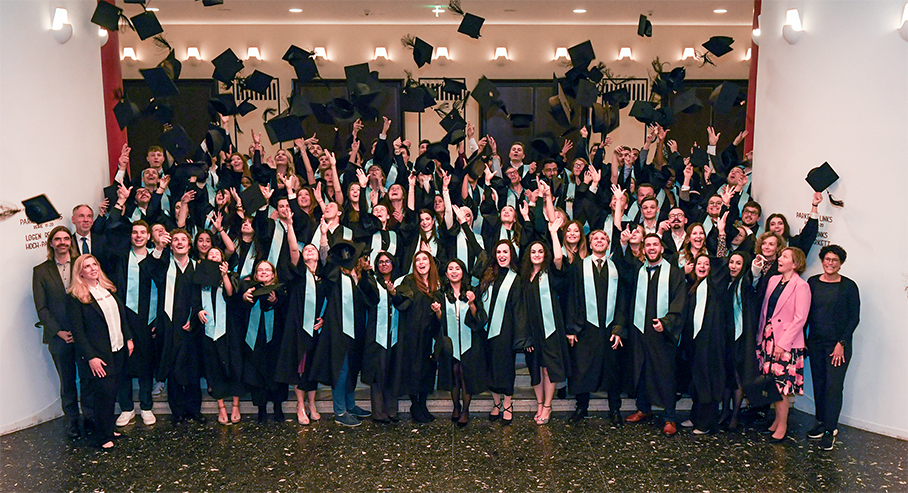 Abolventinnen und Absolventen in schwarzen Roben werfen ihre Hüte in die Luft