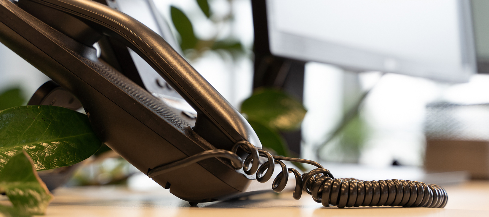 Festnetztelefon im Anschnitt, im Hintergrund sieht man einen Bildschirm