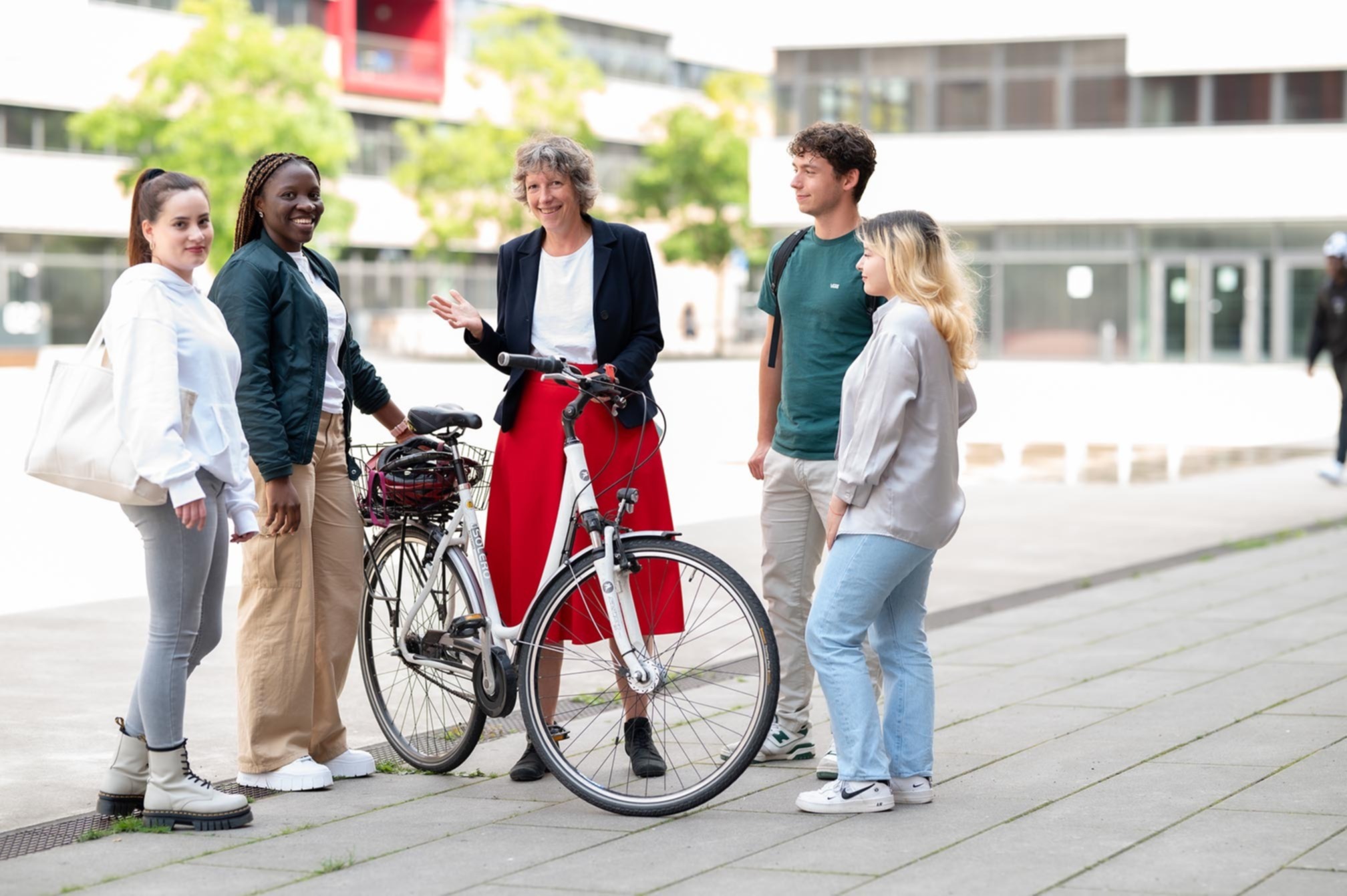 Eine Frau, die ihr Fahrrad hält, spricht mit Studenten auf dem Campus Mülheim.