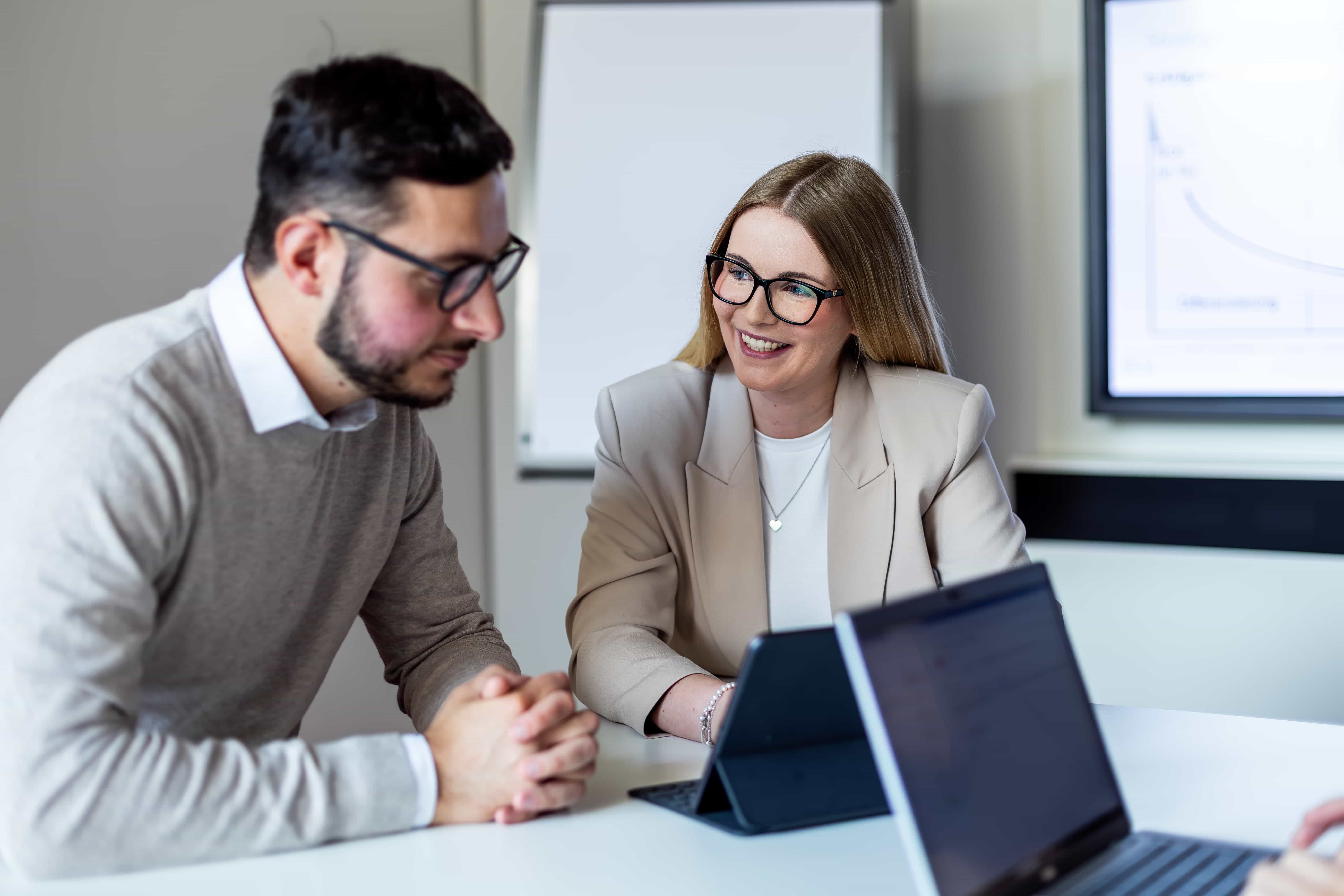 Das Foto zeigt eine weibliche und eine männliche Person, die gemeinsam an einem Laptop sitzen und sich unterhalten.