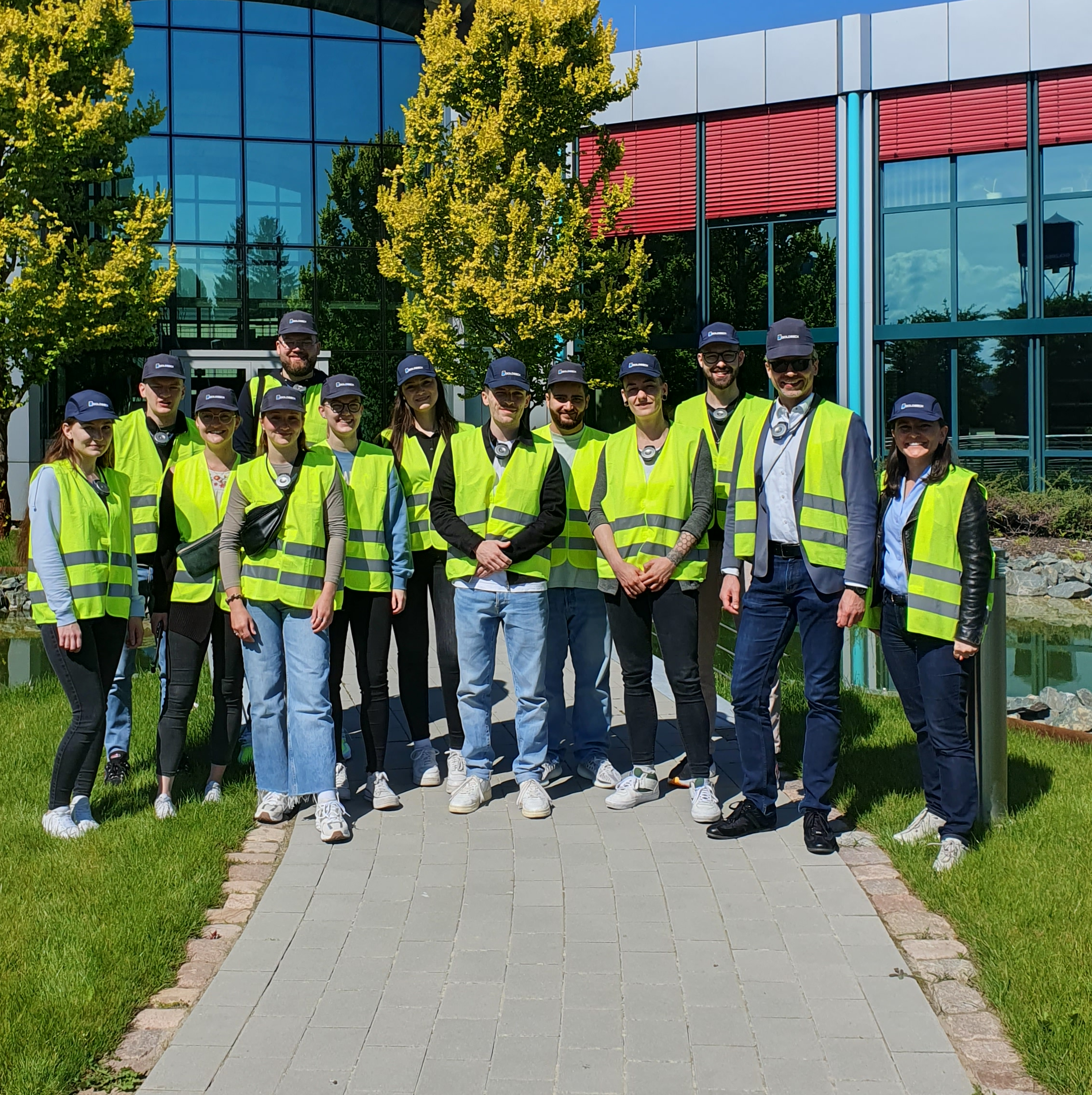 Das Bild zeigt eine Gruppe von 13 Personen in gelben Warnwesten vor einem verglasten Gebäude