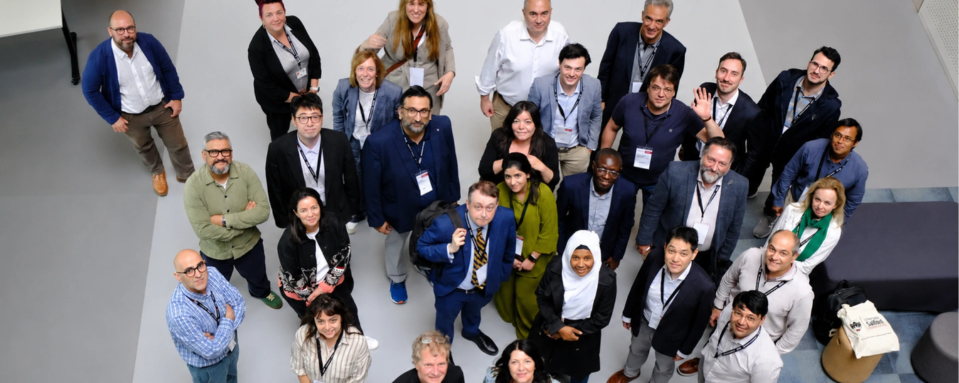 Gruppenfoto der Teilnehmenden der internationalen EPEAI-Konferenz an der University of Salford. Rund 30 Wissenschaftlerinnen und Wissenschaftler aus verschiedenen Ländern blicken von unten fotografiert in die Kamera und stehen in einem hellen Foyer zusammen.