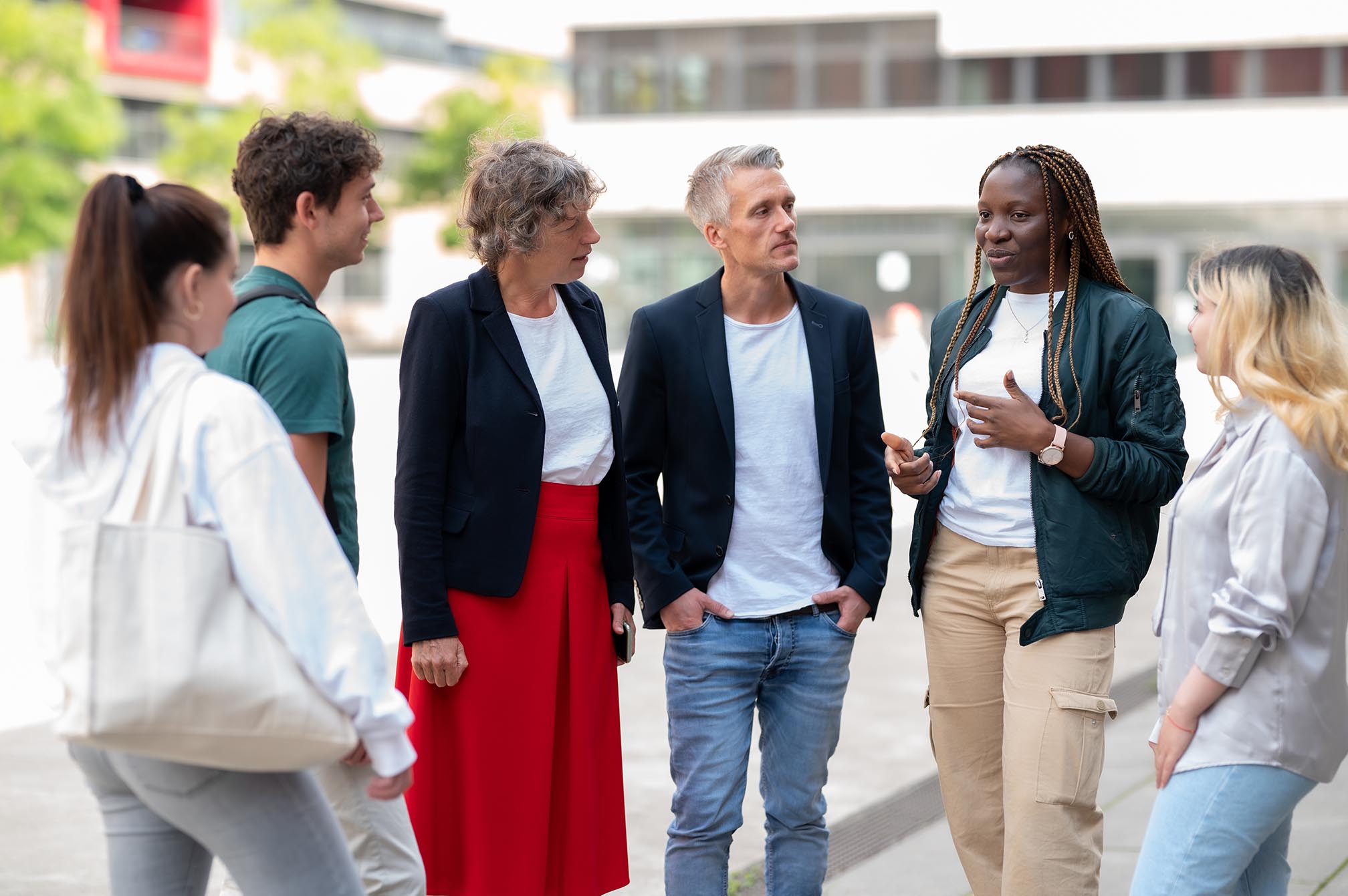 Eine Frau und ein Mann stehen und sprechen mit Studenten auf dem Campus Mülheim.