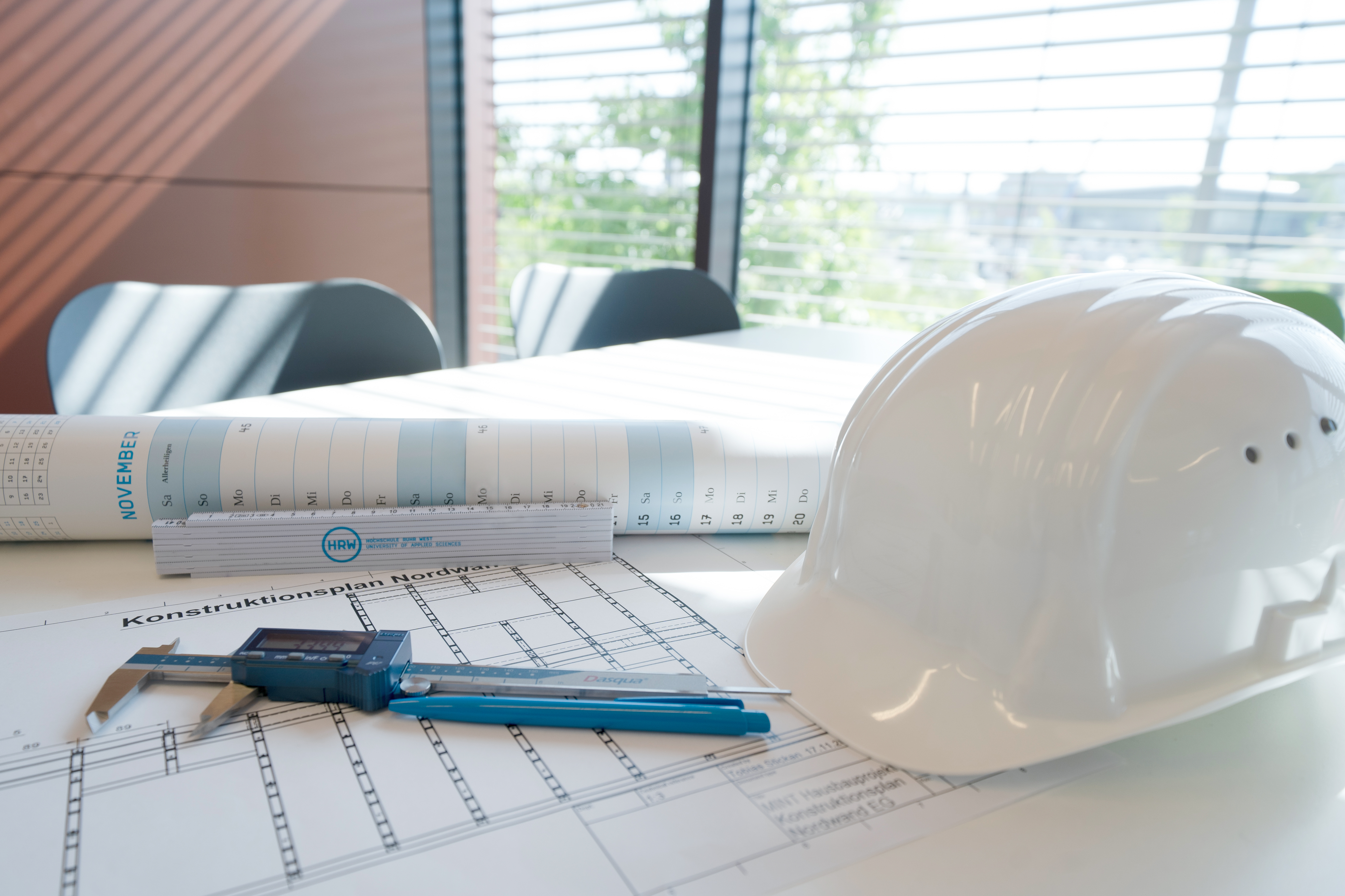 Ein Bauhelm, technische Zeichnungen und ein Zollstock auf einem Besprechnungstisch