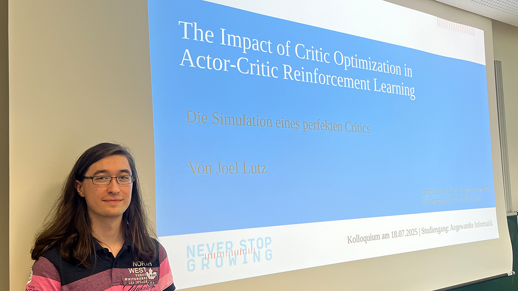 Auf dem Foto ist ein Student zu sehen, der vor einer Leinwand steht. Auf der Leinwand ist die Folie zu sehen, die seine Bachelorarbeit Präsentation zeigt, mit dem Titel "The Impact of Critic Optimization in Actor-Critic Reinforcement Learning".