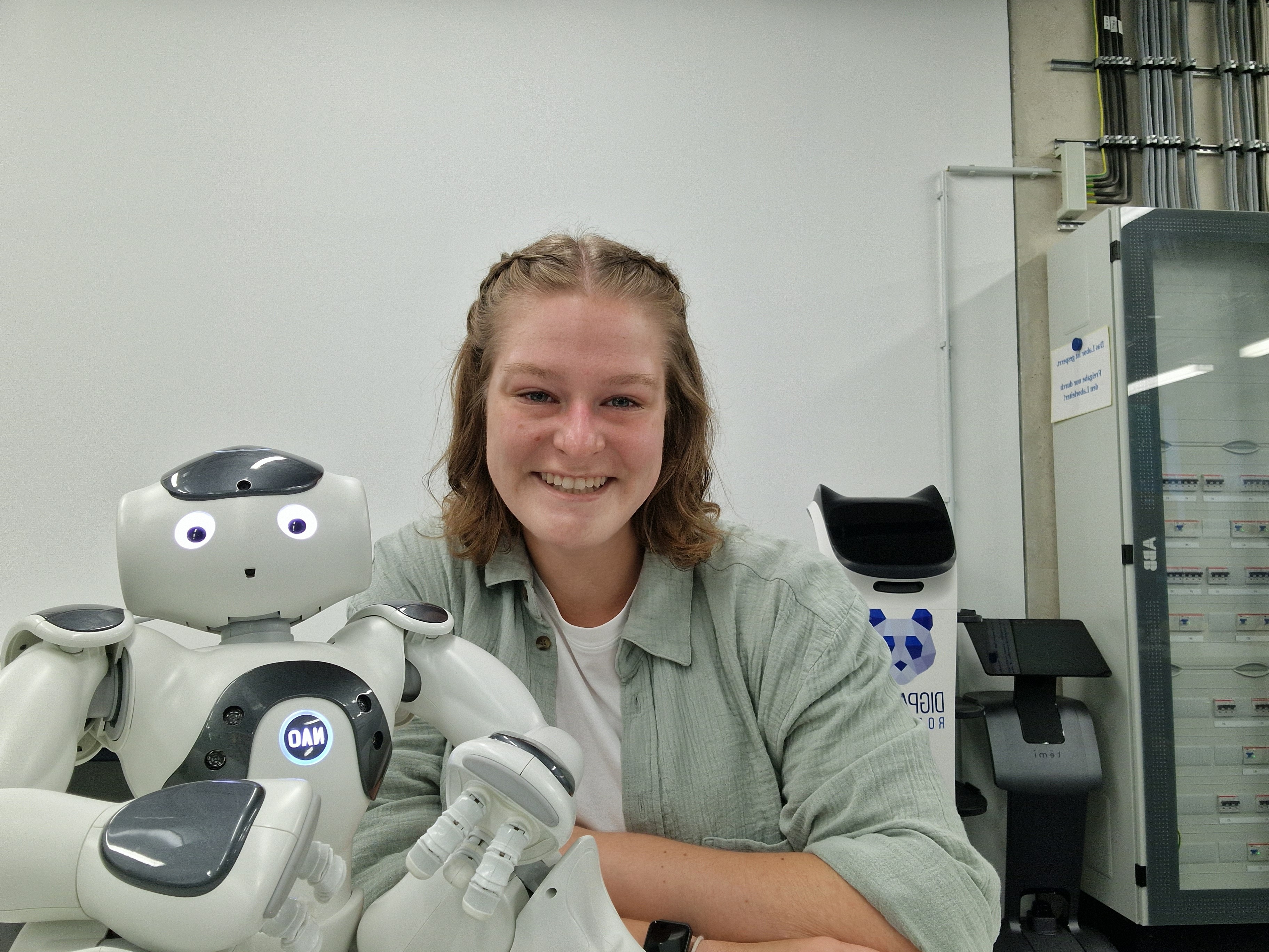 Junge Studentin lehnt sich kameradschaftlich an einen weißen Roboter und lächelt.