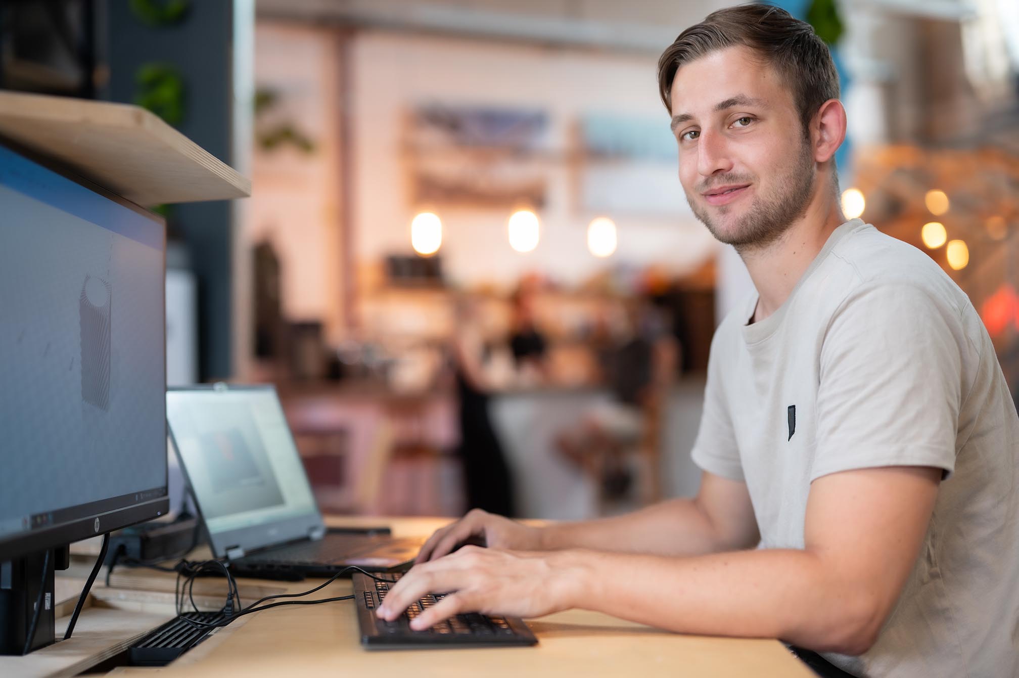 Mann vor dem Laptop; schaut in die Kamera; Hintergrund verschwommen