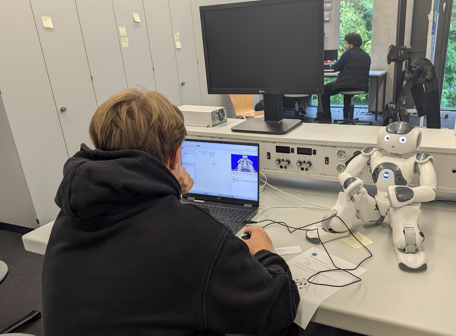 Auf dem Bild ist ein Junge zu sehen, der am Computer die Einstellungen eines kleinen Roboters testet.