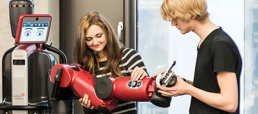 Zwei Personen, die an einem Roboterarm arbeiten.