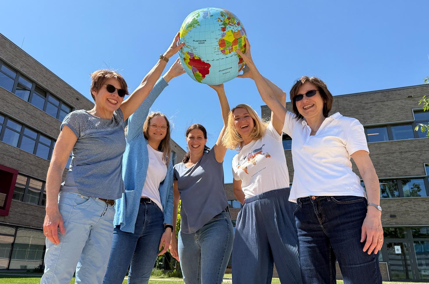 Teamfoto International Office, Mitarbeiterinnen halten einen Globus in der Luft