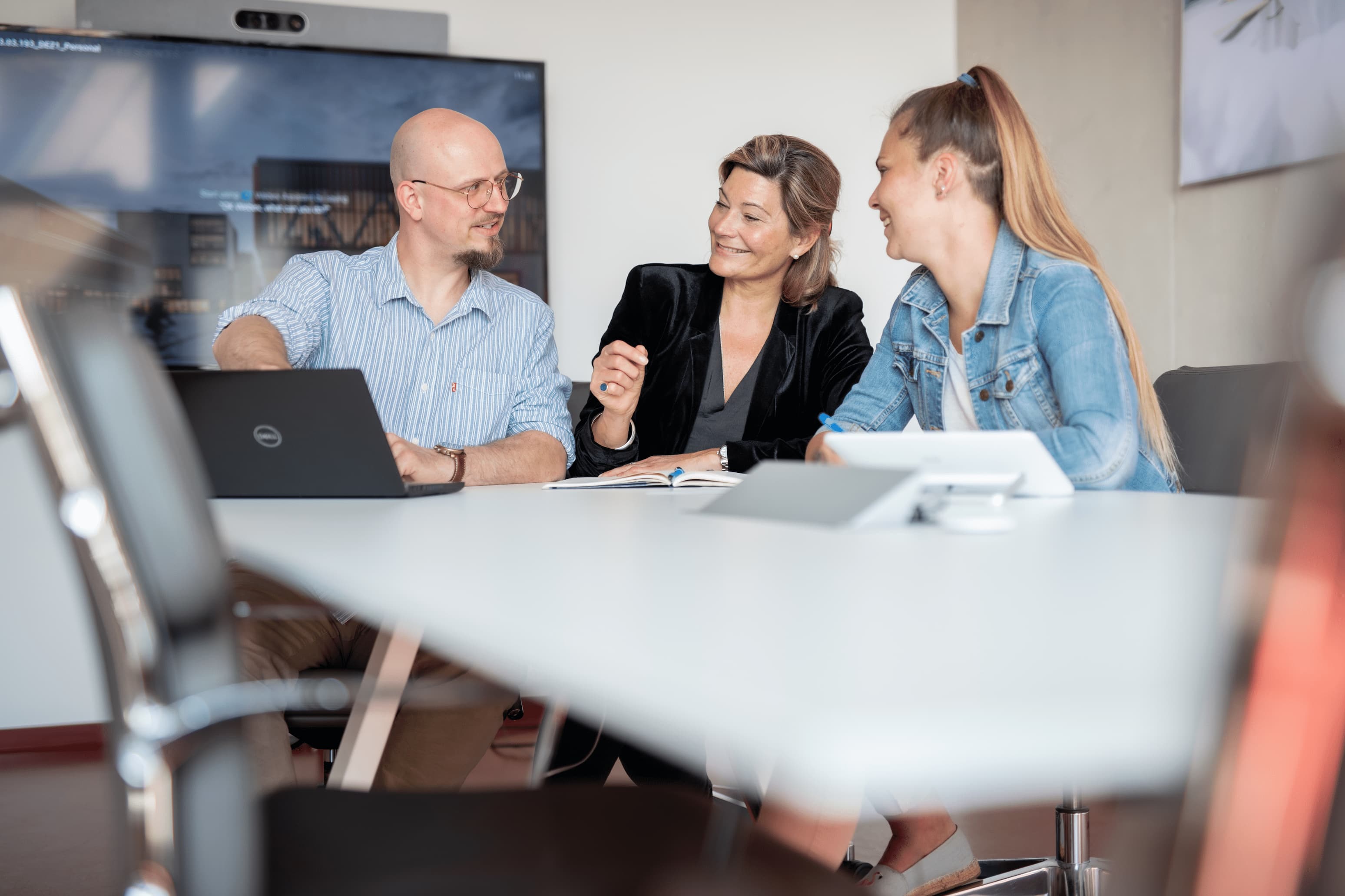 Das Foto zeigt drei Personen, die gemeinsam an einem Tisch sitzen und über Ergebnisse auf einem Laptop sprechen.