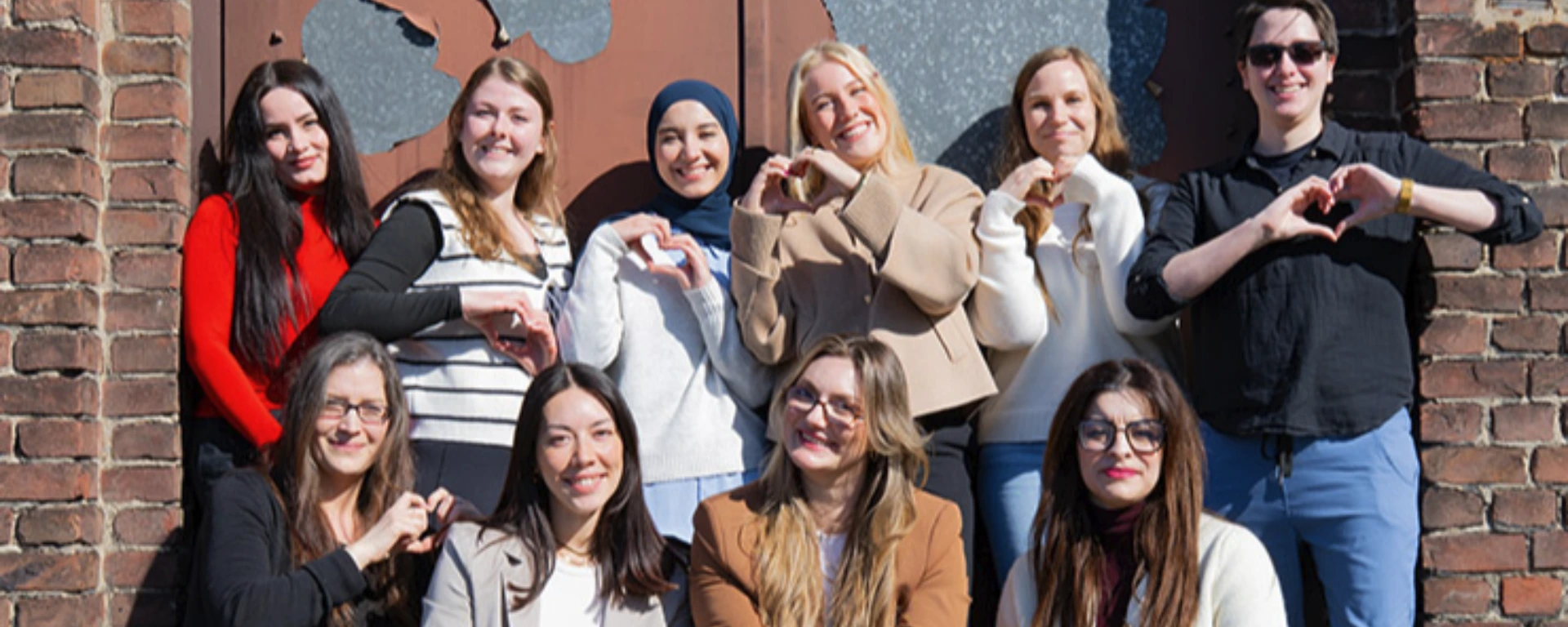 Mehrere Frauen stehen vor einer Backsteinwand und lächeln.
