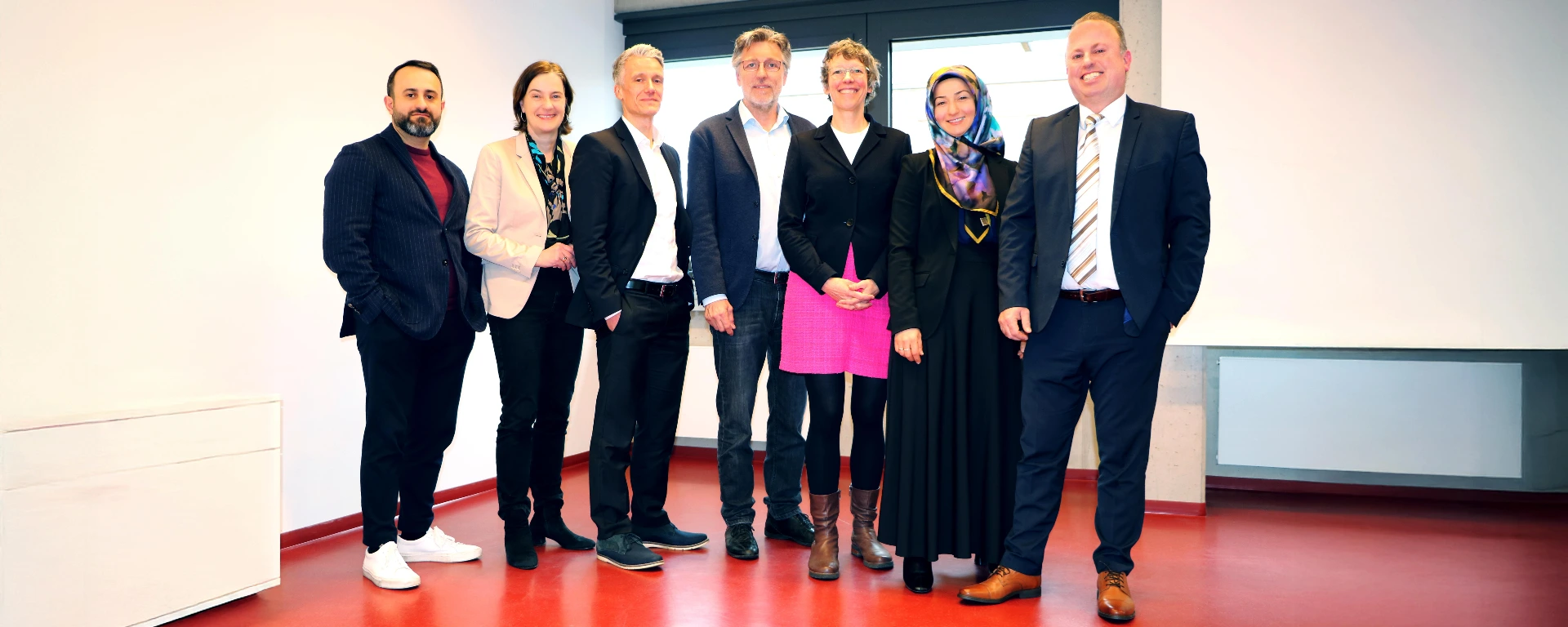 Professionelles Teamfoto einer diversen Arbeitsgruppe in einem modernen Bürogebäude mit hellem Hintergrund und rotem Bodenbelag