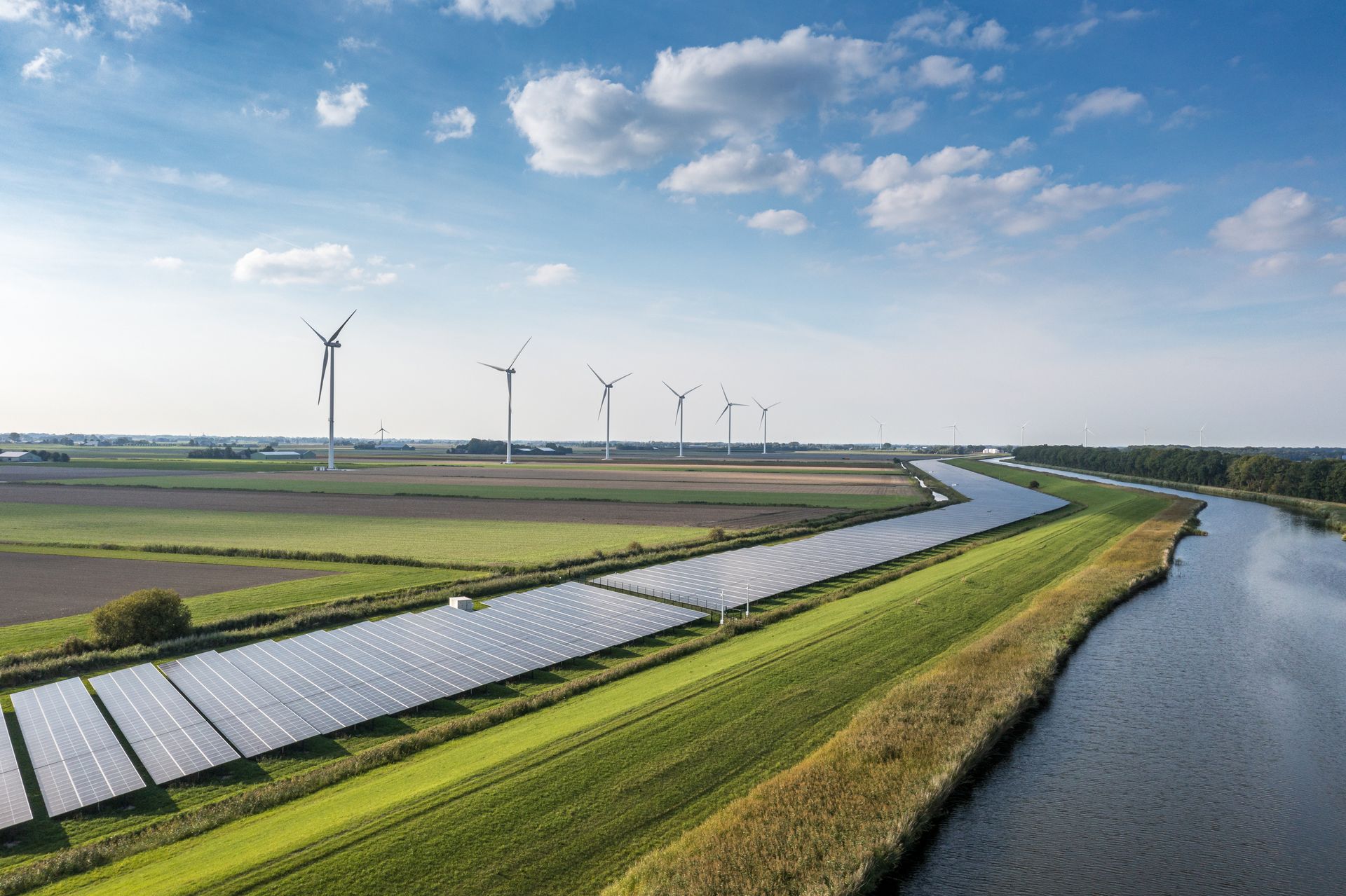 Landschaft mit Solaranlage, Windrädern und Wasserlauf – ein Symbolbild für nachhaltige Energiegewinnung durch Photovoltaik und Windkraft. Das Motiv steht für Energiewende, Umwelttechnik und erneuerbare Energien.