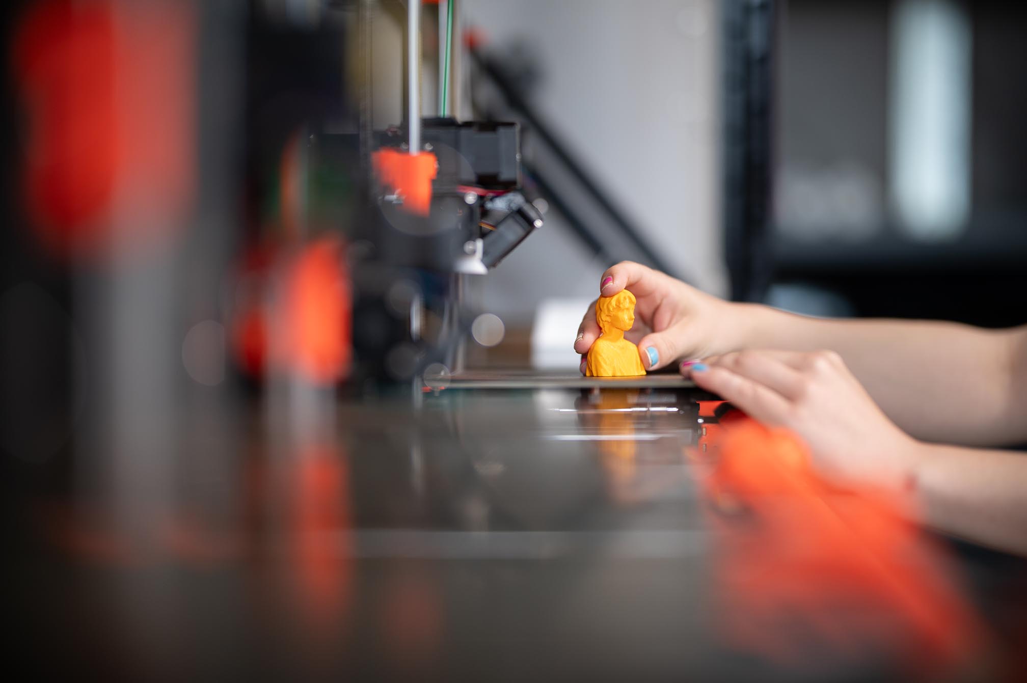 Eine Person nimmt ein 3D-gedrucktes Objekt vom Druckbett eines 3D-Druckers.