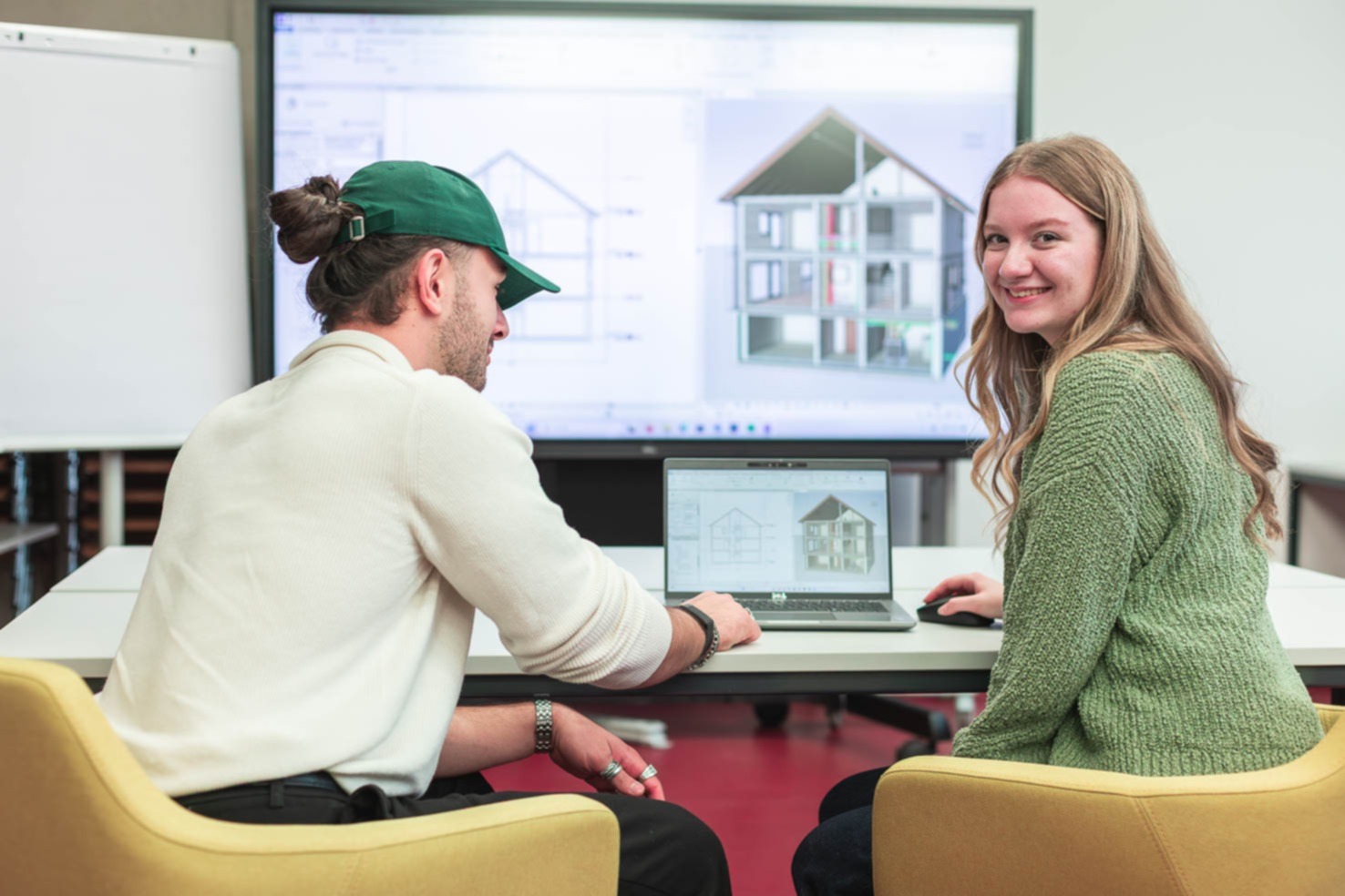 Zwei Studierende sitzen an einem Laptop und bearbeiten die 3D Ansicht eines Bauwerks am Computer