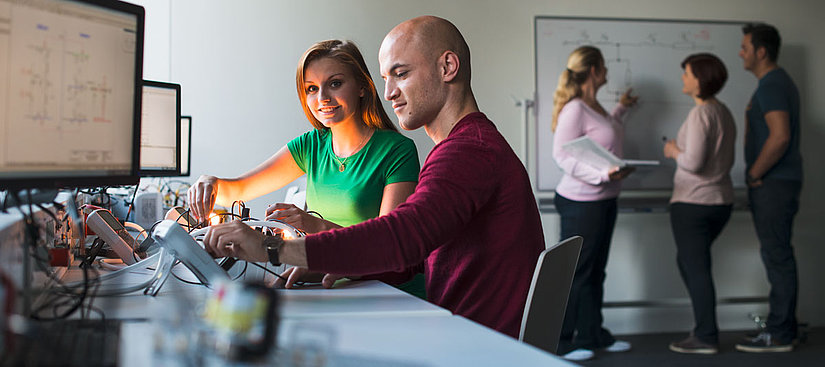 Zwei Personen sitzen an einem Tisch und arbeiten mit elektrischen Geräten