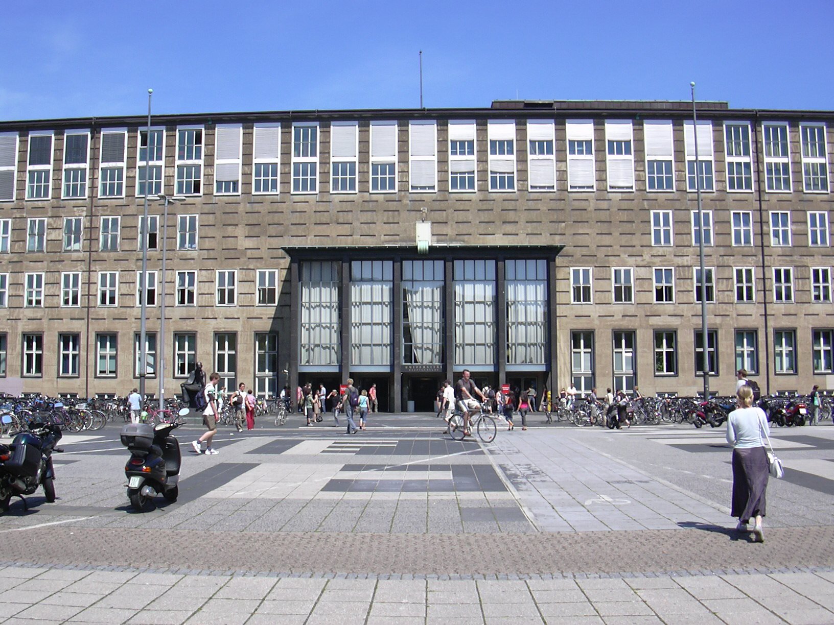 Großes Gebäude mit vielen Fenstern aus hellbraunen Stein. Architekturelement sind durchweg geradlinig.