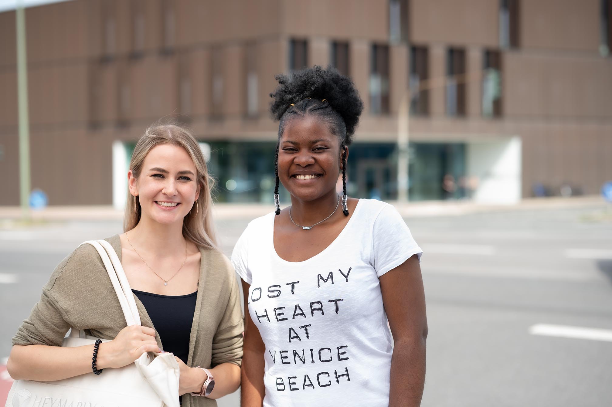 Zwei Frauen schauen direkt in die Kamera und lächeln vor dem Campus Bottrop.