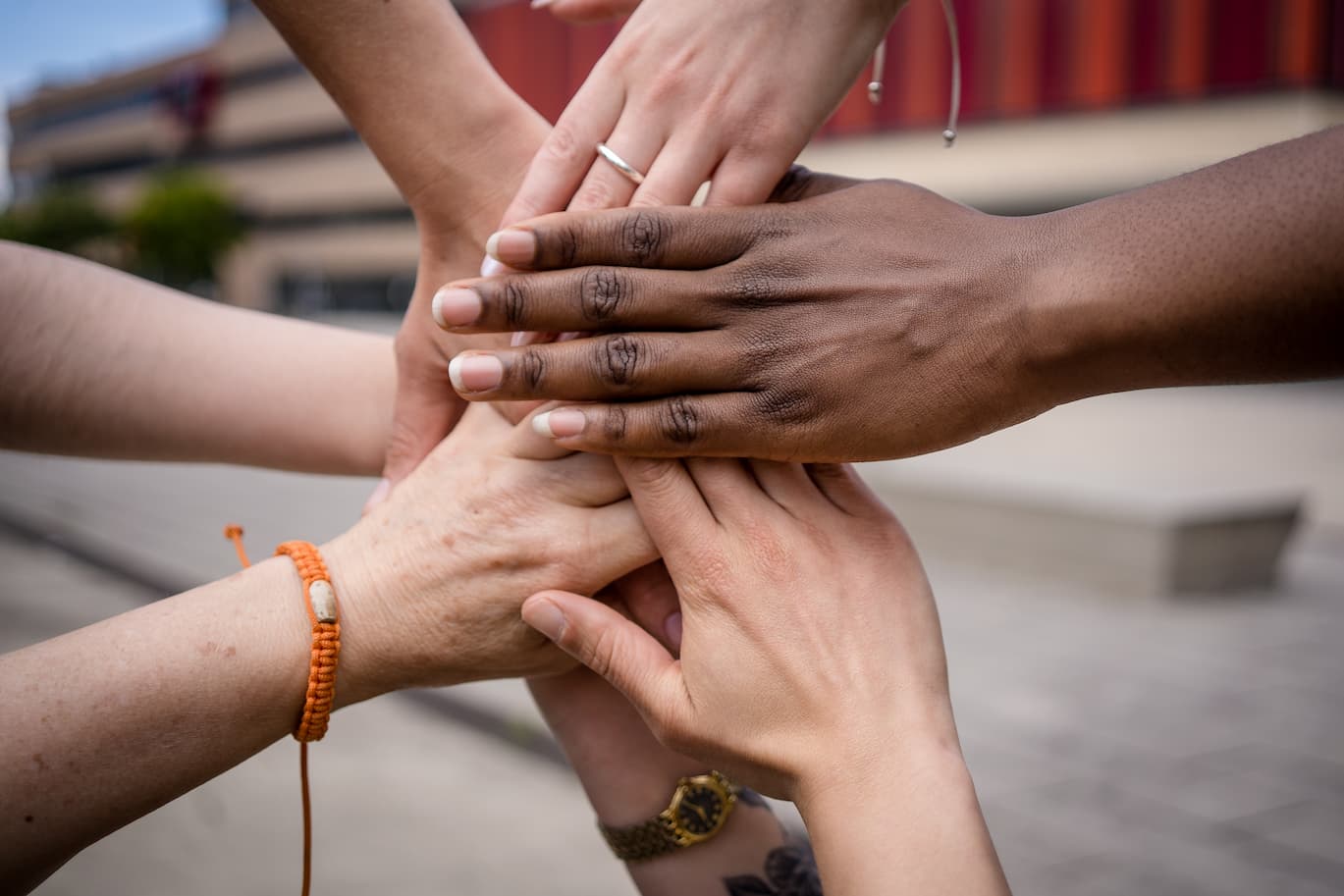 Mehrere Hände unterschiedlicher Personen liegen übereinander und bilden einen gemeinsamen Stapel, als Zeichen für Zusammenhalt und Teamwork.
