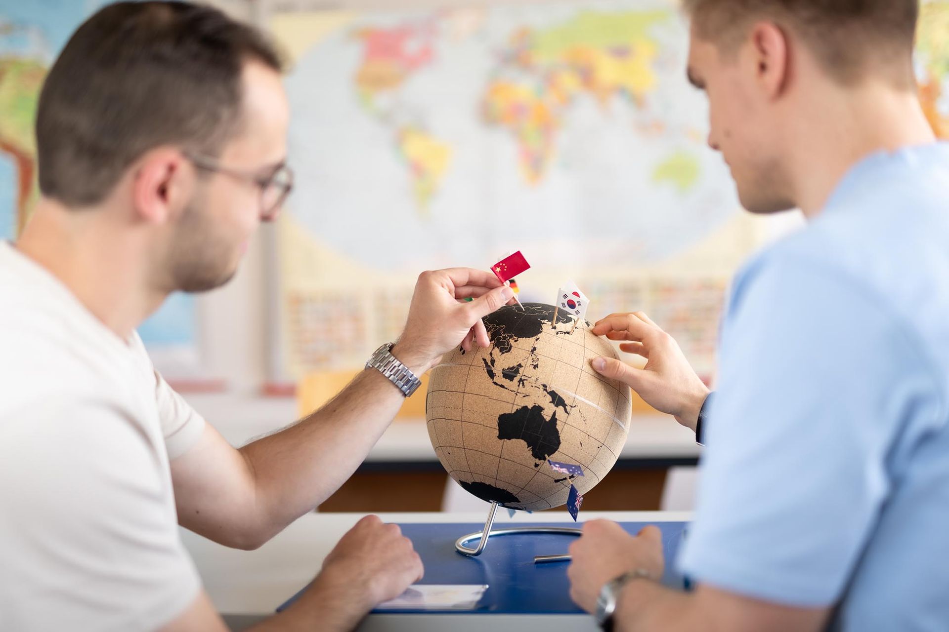 Zwei Studierende der Hochschule Ruhr West markieren internationale Standorte auf einem Globus. Das Bild steht exemplarisch für die globale Ausrichtung, Austauschprogramme und die internationale Vernetzung der HRW.