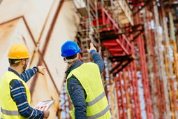 Zwei Ingenieure auf einer Baustelle, die auf ein Baugerüst zeigen.