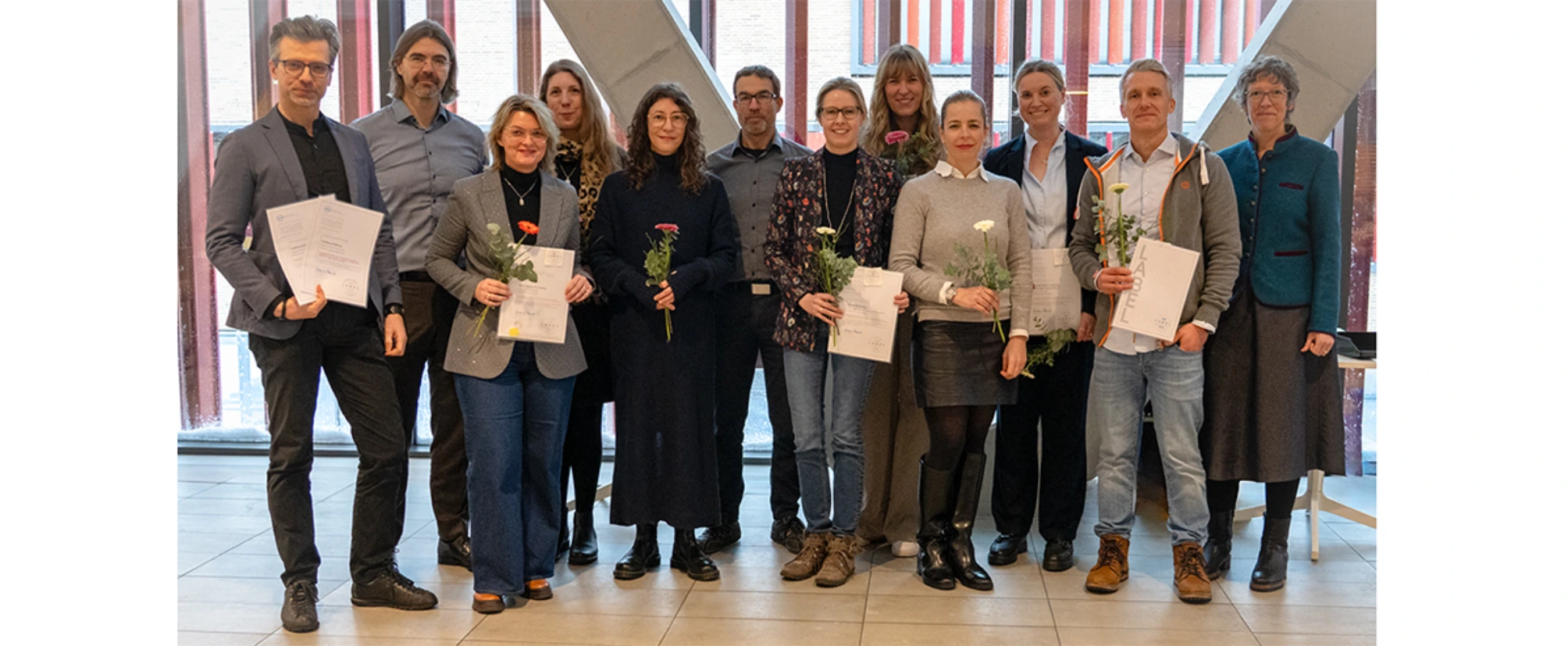 Merere Frauen und Männer stehen aufgereiht und halten Urkunden und eine Blume in der Hand.