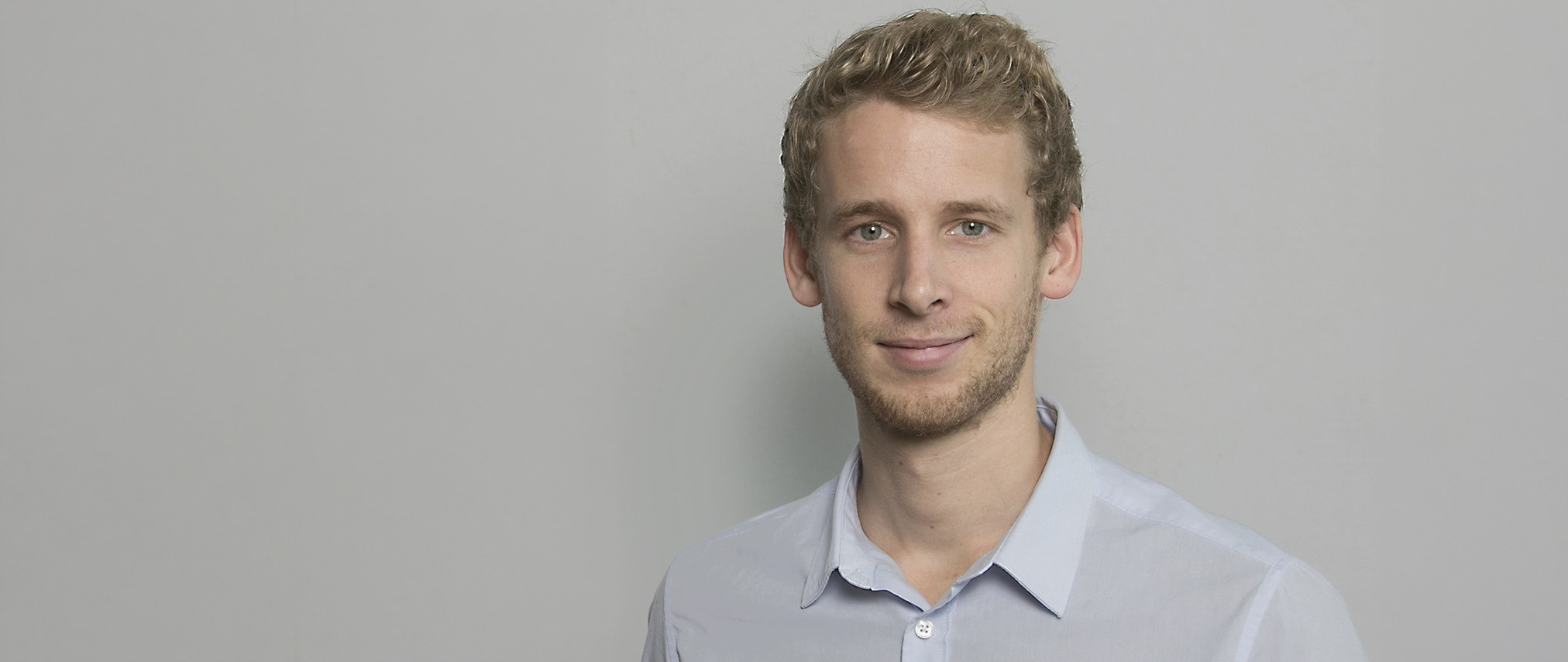 Junder Mann mit Bart vor einer hellen Wand.