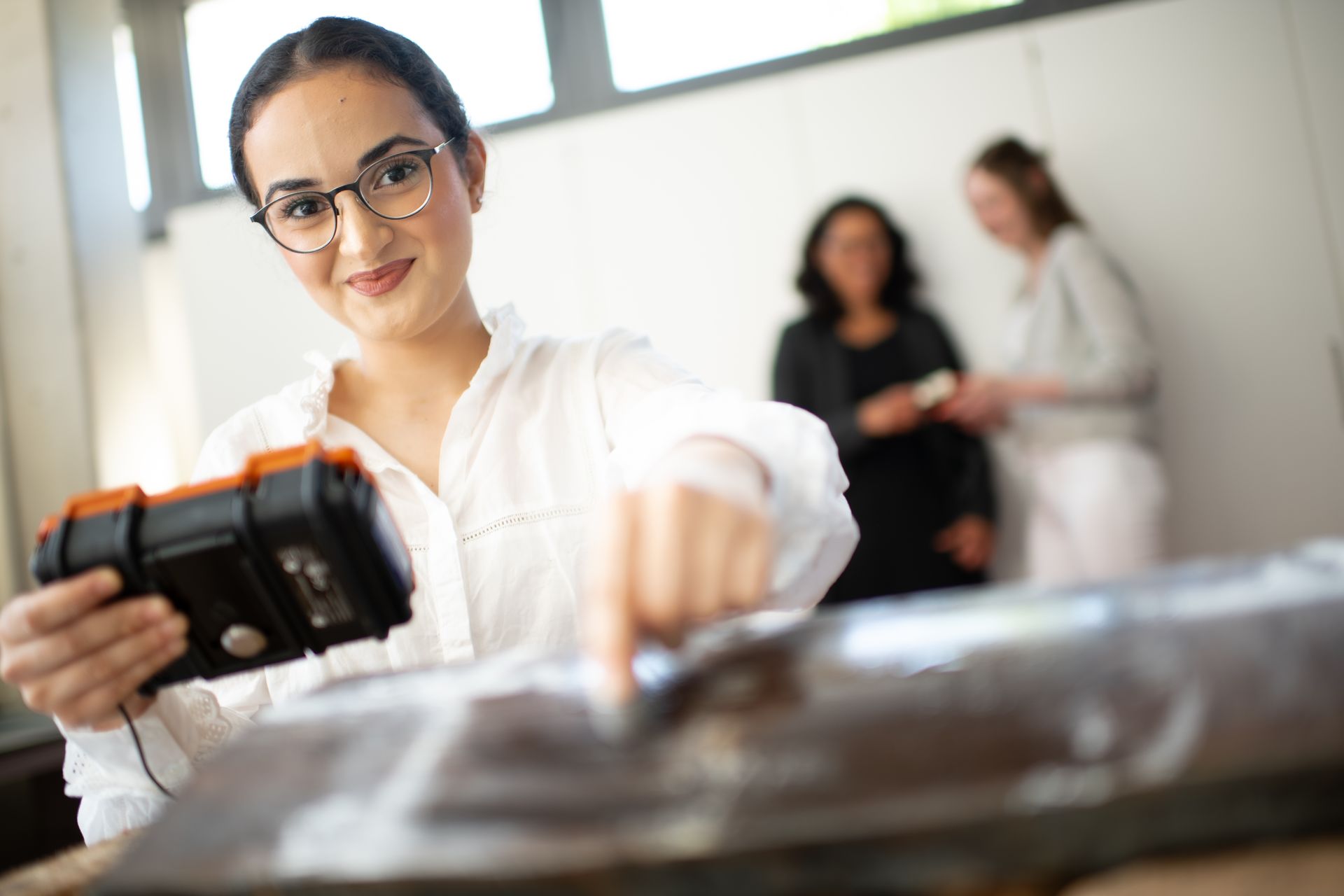 Eine Studentin der Hochschule Ruhr West führt eine Werkstoffprüfung mit einem mobilen Prüfgerät auf einer Metalloberfläche durch. Die praxisnahe Lehre an der HRW vermittelt Grundlagen in Materialanalyse und Qualitätssicherung.