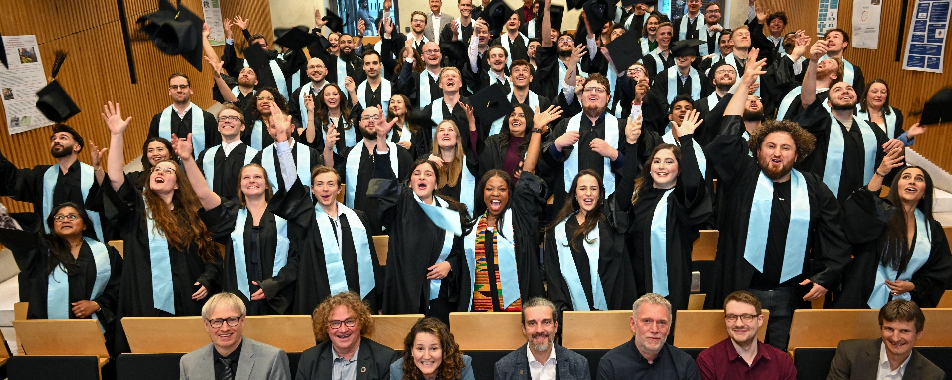 Studentinnen und Studenten in ihren schwarzen Roben werfen ihre Hüte in die Luft.