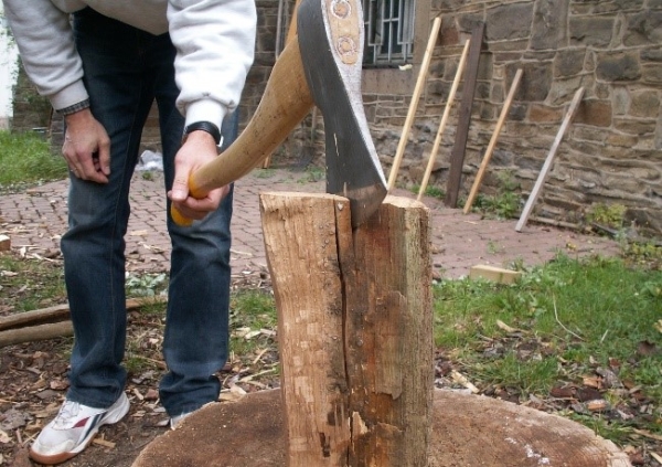 Das Bild zeigt eine Person die eine Axt auf einem Holzscheit hält