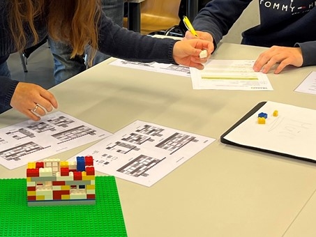 Das Bild zeigt die Hände von zwei Personen, die Prozesse optimieren. Ebenfalls zu sehen ist ein Block aus Lego-Steinen