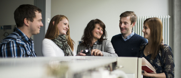Eine Gruppe von fünf Leuten darunter 2 Männer und 3 Frauen die zusammen am Tisch sitzen und miteinander lachen.