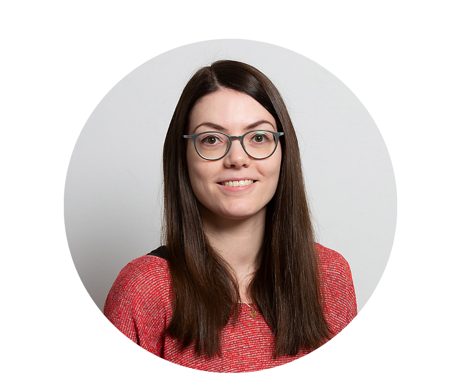 Eine junge Frau mit langen, dunklen Haaren und einer roten Brille in einem korallroten Pullover.