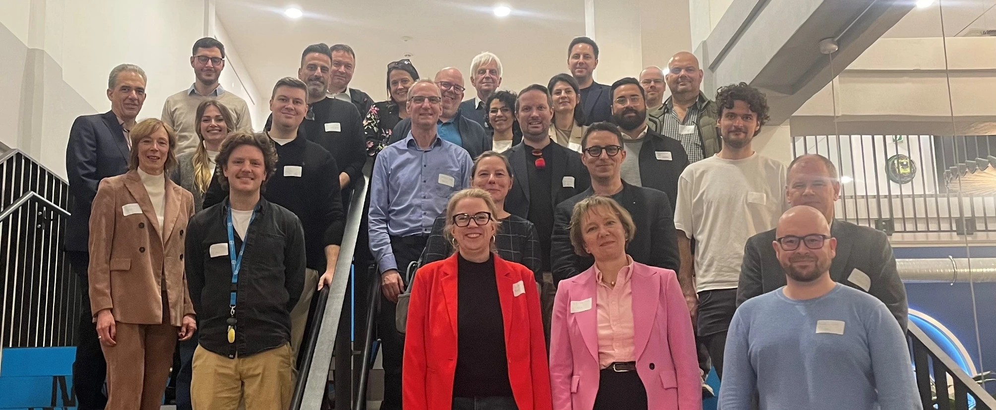 Gruppenfoto der Teilnehmenden eines Austauschs zu k&uuml;nstlicher Intelligenz, die gemeinsam auf einer Treppe im Geb&auml;ude stehen und f&uuml;r ein Foto posieren.