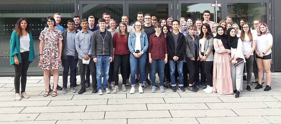 Eine Gruppe von Menschen stehen glücklich vor einem Gebäude und lasse sich Fotografieren