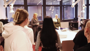 KKS Smart Health Lab / Szene im Labor; Im Vordergrund eine Gruppe junger Frauen, die den Ausf&uuml;hrungen zweier junger Frauen im Hintergrund zuh&ouml;ren.