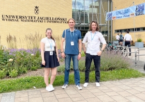 Zwei Männer und einer Frau vor einer kleinen Grünfläche, die zu dem gelben Universitätsgebäude gehört, in dem die Konferenz stattfindet.